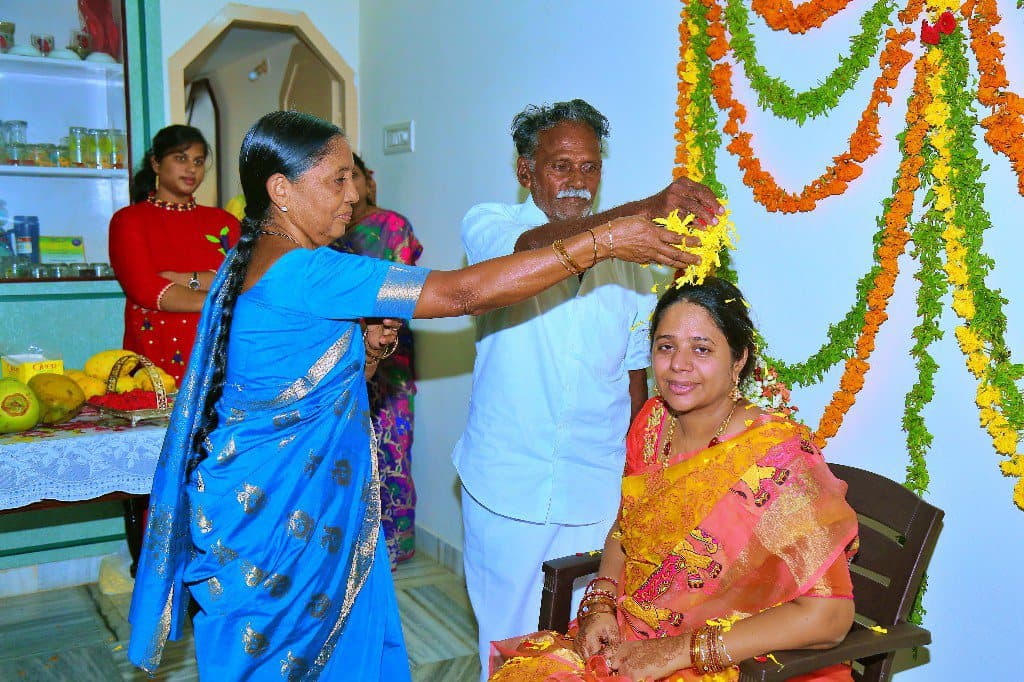 Family elders performing a blessing during a home ceremony beneath flower garlands.