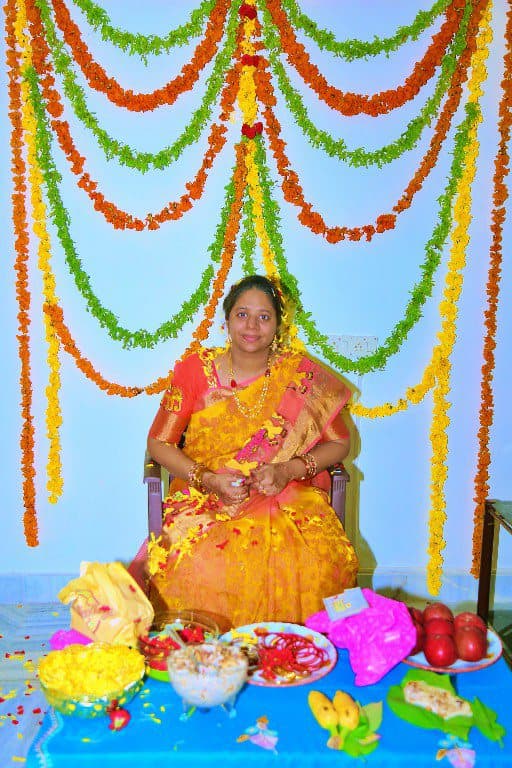 An expectant mother seated beneath strung marigold garlands during a seemantham ceremony.