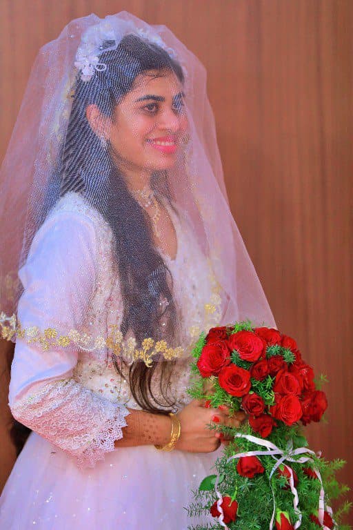 A bride in a white gown and veil holding a bouquet of red roses.