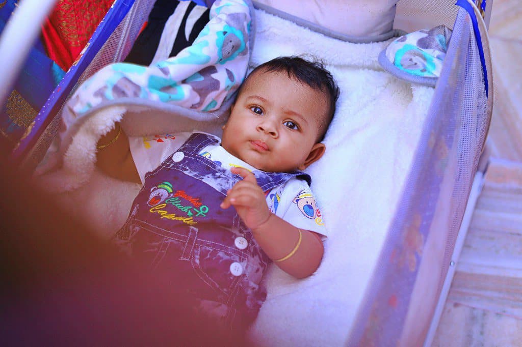 A baby lying in a bassinet, looking towards the camera.
