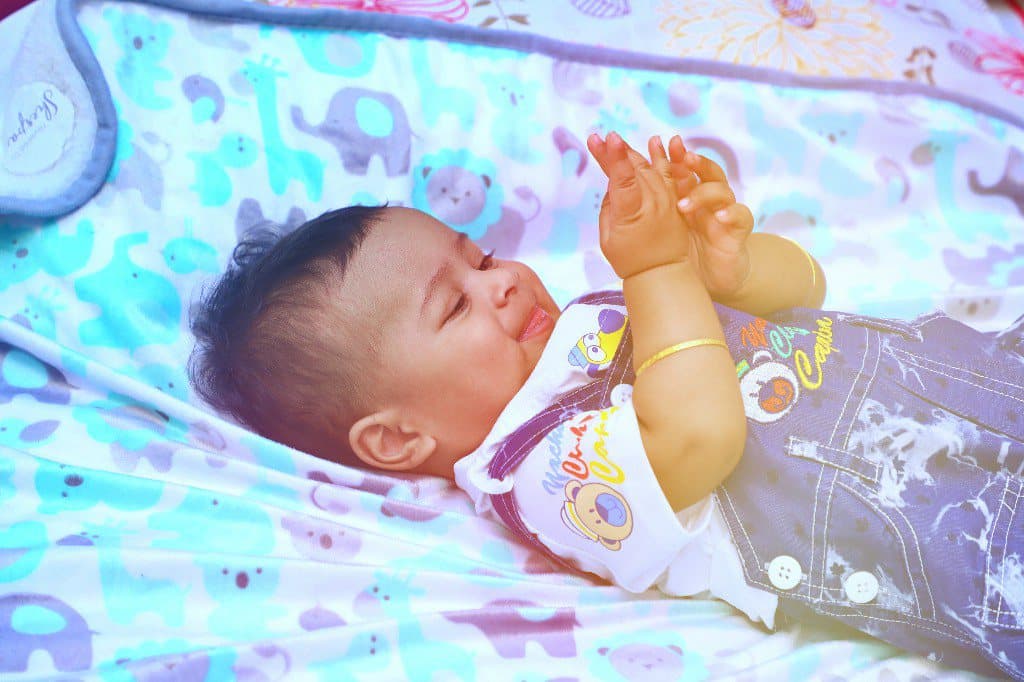 A newborn lying on a patterned blanket with arms raised.