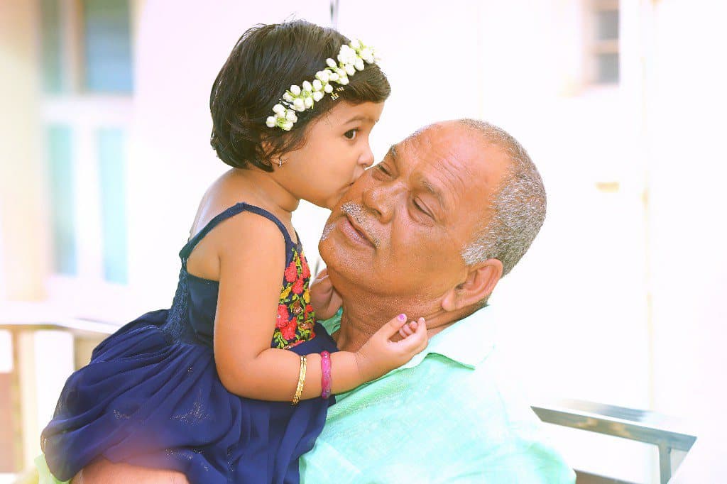 A small girl in a floral headband kissing her grandfather on the cheek.