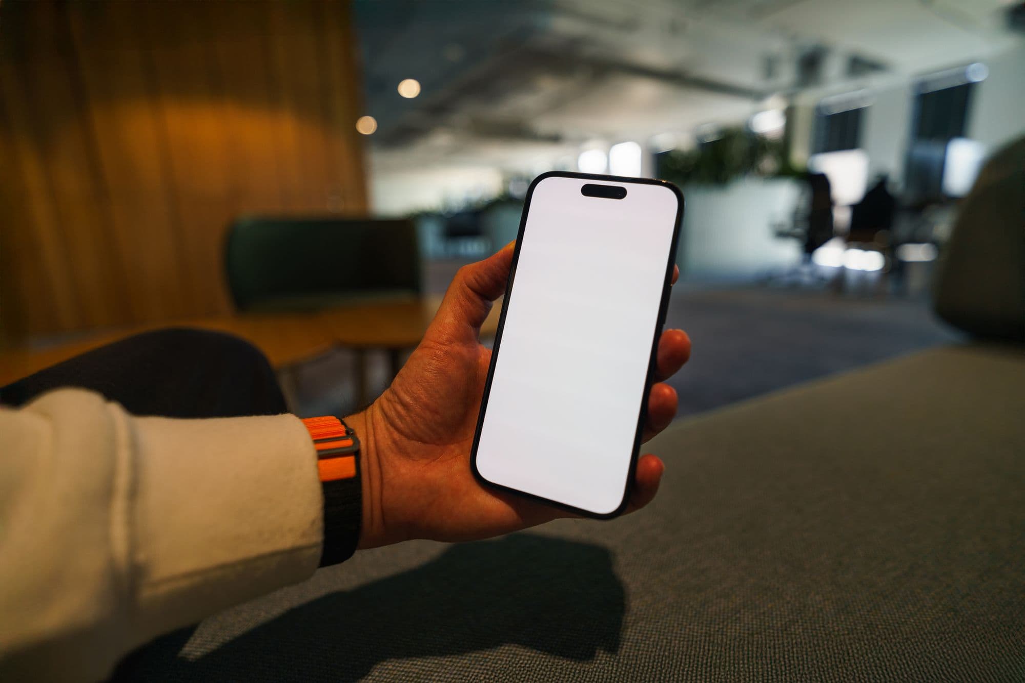 A hand holding a smartphone in a modern office.
