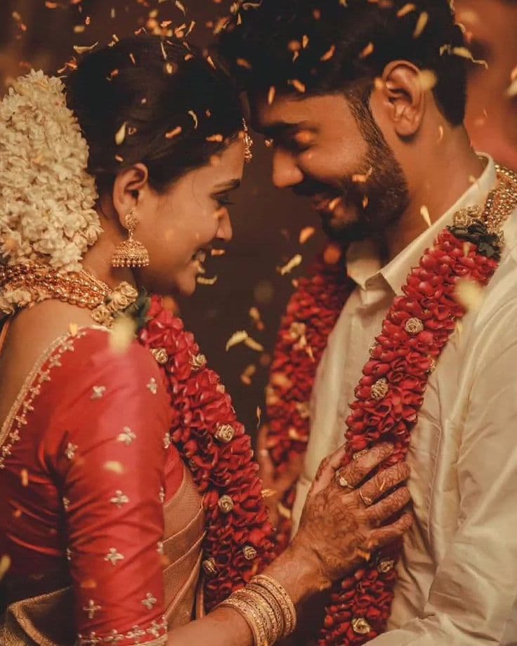 A wedding couple in flower garlands beneath falling petals.